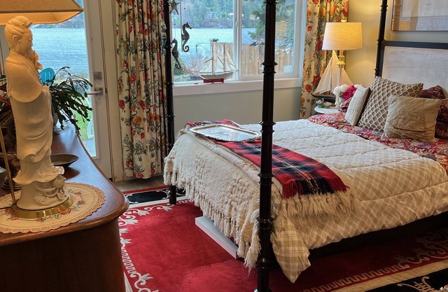 Four-poster bed with a quilted cover, floral curtains, and a view over the water