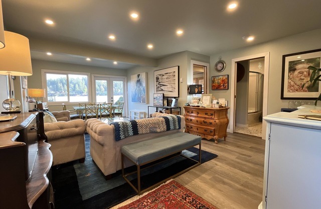 Two soft sofas and a bench facing framed art, with a dining table by the windows